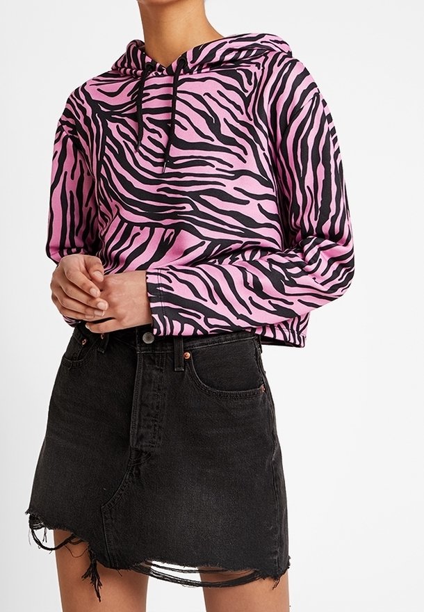Persona che indossa una felpa con stampa zebra rosa e nera abbinata a una mini gonna di jeans nera con effetto usurato.
