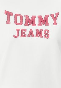 Camiseta blanca con el texto "TOMMY" y "JEANS" en rojo bold y un acabado desgastado. Hecha de algodón con una textura suave.