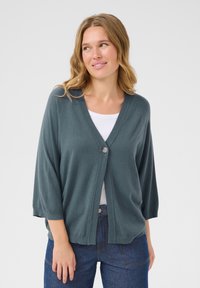 Cardigan teal avec un décolleté en V profond, des manches trois-quarts et une fermeture à un bouton. Texture douce avec des bords côtelés et coupe décontractée.