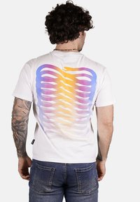 Maglietta bianca con un motivo a gradiente multicolore in viola, arancione e giallo sul retro. Maniche corte, vestibilità rilassata e materiale in cotone.