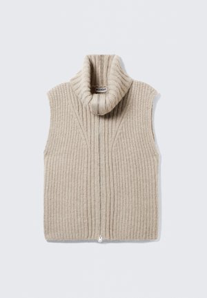 Beige gestrickte ärmellose Weste mit hohem Kragen, vertikaler Rippstruktur und einem Reißverschluss auf der Vorderseite. Etikett im Kragen sichtbar.