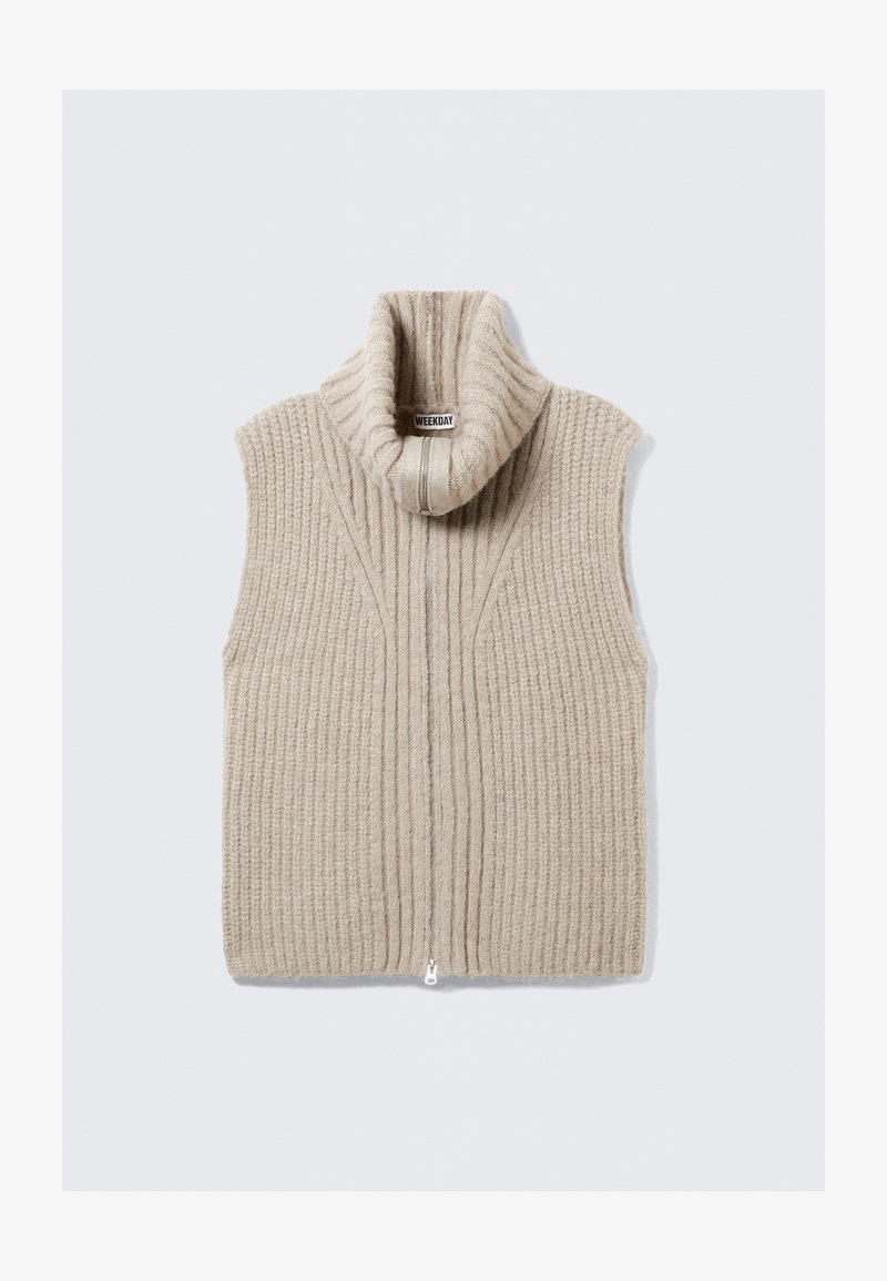Gilet sans manches en tricot beige avec un col haut, présentant une texture côtelée verticale et une fermeture éclair à l'avant. Étiquette visible à l'intérieur du col.