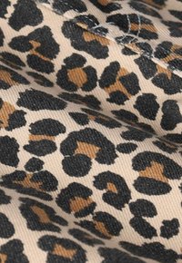 Tissu à imprimé léopard avec des taches noires et brun doré sur fond crème, mettant en valeur un design texturé et graphique.