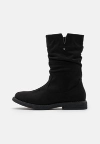 Bottines noires en suède doux avec un design ample. Elles disposent d'un talon bas, d'un bout arrondi et d'une fermeture éclair agrémentée d'un bouton-pression.