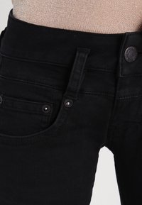 Jeans neri con un design aderente, caratterizzati da una vita a media alta, tasche anteriori e tessuto testurizzato. Dettaglio con bottone in metallo in vita.