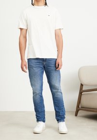 Vit bomulls t-shirt med en liten logotyp, kombinerad med blå denimjeans och vita sneakers. Enkelt design, avslappnad passform och utan mönster.