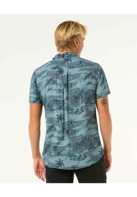 Korte mouwen shirt in lichtblauw met een donkere palmboomprint. Heeft een rugstuk met een plooi en een rechte zoom. Gemaakt van lichtgewicht stof.