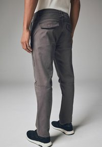 Graue Baumwollhosen im Slim-Fit-Stil mit flachen Taschen und glatter Textur. Getragen mit schwarzen Sportschuhen vor einem neutralen Hintergrund.