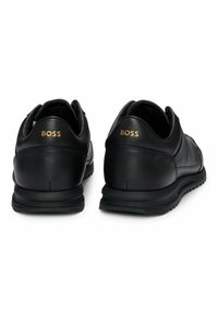 Czarne skórzane trampki z teksturowanym wzorem, gumową podeszwą i wyeksponowanym logo na pięcie. Okrągły kształt z wyściełanym kołnierzem.