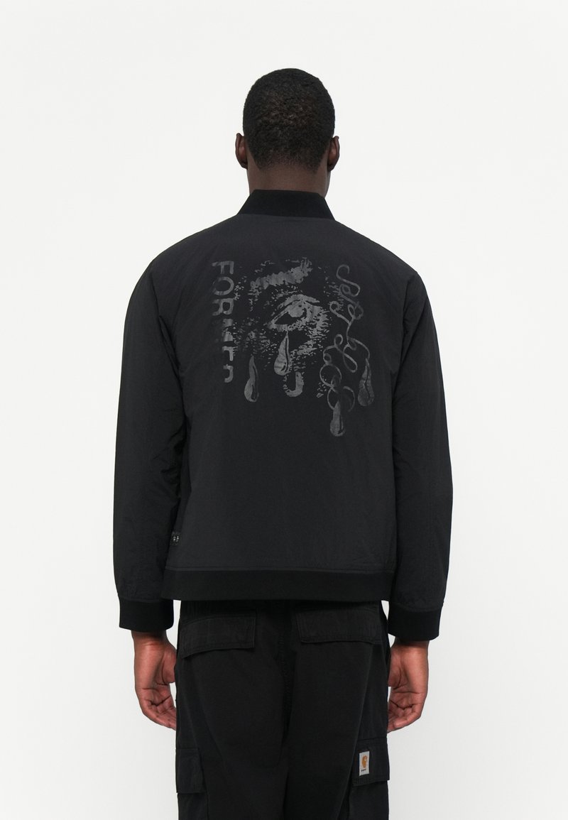 Black bomber jacket with a matte finish, featuring a large graphic print on the back, text, and a ribbed collar and cuffs. Casual fit.