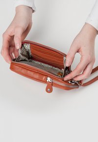 Tan leren portemonnee met ritsluiting, uitgerust met meerdere kaarthouders, een gestreepte binnenvoering en een afneembare riem voor veelzijdigheid.