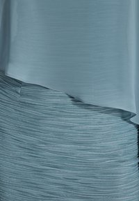 Robe bleu clair avec une couche supérieure lisse et transparente et une jupe texturée plissée, ornée de délicates accents scintillants.