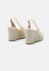 Bež sandale na klin z vrvico, s peto ovito z jutovino, zgornjim delom iz teksturirane tkanine in zaobljenim nosom, ki prikazujejo preprost dizajn in nevtralno barvo.