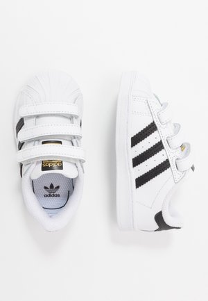 Weiße Adidas Kleinkind-Sneaker mit schwarzen Streifen, drei Klettverschlüssen und Muschelzeh-Design, von oben und von der Seite dargestellt.