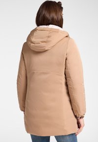 Beige prošívaný kabát s kapucí, vybavený elastickými manžetami a hladkým povrchem. Design je středně dlouhý, až po stehna, a má jednoduchou siluetu.