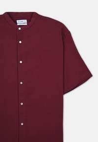 Camicia bordeaux a maniche corte con colletto alla coreana, caratterizzata da un tessuto testurizzato e bottoni in argento lungo la parte anteriore per la chiusura.