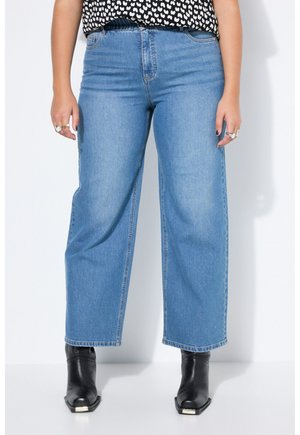 Kvinde iført lyseblå jeans med vide ben, sorte ankelstøvler med firkantede tåspidser og en sort top med hvide hjerte-mønstre.