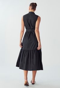 Abito in cotone nero con colletto, design senza maniche, vita cintrata e orlo arricciato a strati lungo la caviglia. Texture liscia.