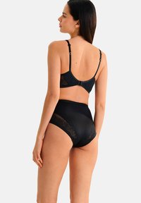 Zwarte lingerieset met een zacht hemdje voorzien van bloemenkant details en een slip met hoge taille en doorschijnende kantaccenten aan de zijkanten.