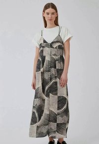 Vestido maxi com suspensórios, apresentando um padrão abstrato preto e creme, botões à frente e um corte descontraído. Material em algodão.