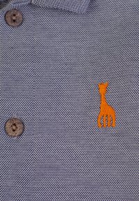 Polo shirt navy con tessuto testurizzato, due bottoni scuri e logo di una giraffa ricamato arancione sul lato sinistro del petto.