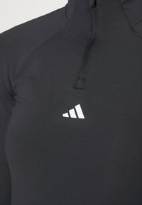 Schwarzes sportliches Viertel-Reißverschluss-Oberteil aus dehnbarem Material, mit kurzem Reißverschluss und weißem Adidas-Logo mit drei Streifen auf der linken Brust.
