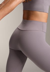 Grå, högmidjade leggings tillverkade av elastiskt tyg, med en slät textur och en minimalistisk design med en logotyp på midjebandet.