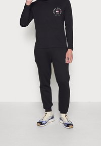 Musta pitkähihainen paita ja housut, joissa on logokuvio, yhdistettynä vaaleisiin lenkkikenkiin, joissa on sinisiä yksityiskohtia ja teksturoitu pohja.