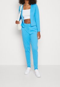 Ljusblå blazer och matchande byxor i mjukt tyg, tillsammans med en vit crop top och vita sneakers. En liten vit väska bärs crossbody.