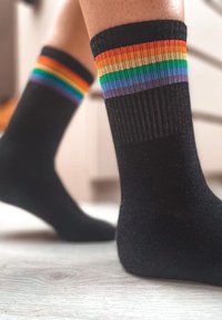 Calcetines negros con un patrón de rayas coloridas en naranja, amarillo, verde, azul y púrpura en el puño, hechos de una tela texturizada y suave.
