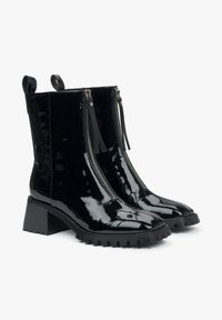 Zwarte gepatineerde leren enkellaarsjes met een chunky hak, voorzien van dubbele ritssluitingen aan de voorkant en kwastjes. Getextureerde rubberen zool.