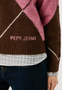Bruine en roze gebreide trui met ruitpatronen, voorzien van een geribbelde zoom en de merknaam "PEPE JEANS" in het roze geborduurd.