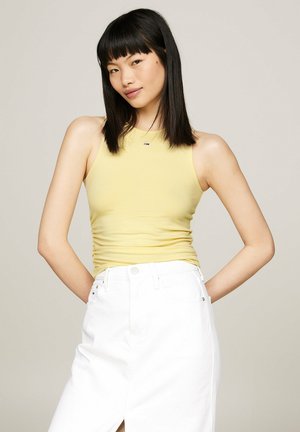Top ajustado amarillo con escote redondo y detalle fruncido en el costado, combinado con una falda de mezclilla blanca de tiro alto con una abertura en la parte frontal.