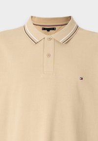 Polo shirt beige a maniche corte con due bottoni, colletto a righe e piccolo logo ricamato di Tommy Hilfiger sul petto.
