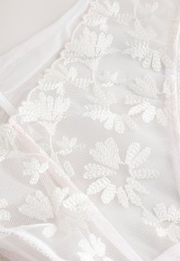 Tissu en dentelle blanche transparente avec une broderie florale délicate, doté d'une texture douce et d'éléments de design subtilement transparents.