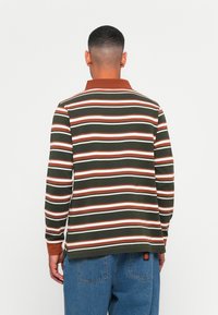 Donkergroene longsleeve polo met horizontale strepen in het wit, oranje en bruin. Voorzien van een bruine kraag en geribde manchetten.