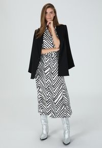 Schwarz-weiße Zickzack-mustered Kleid mit tailliertem Design, kombiniert mit einem schwarzen Blazer und glänzenden silbernen kniehohen Stiefeln.