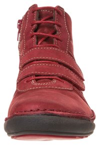 Chaussure en cuir rouge avec lacets et bandes Velcro, bout arrondi et semelle en caoutchouc noir. Présente des coutures contrastées et une fermeture éclair sur le côté.