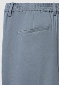 Pantaloni azzurri chiari, texture con vita elastica e una singola tasca posteriore. Il tessuto presenta un sottile motivo a spina di pesce.