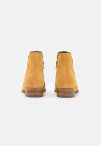 Botas de tobillo amarillas hechas de cuero perforado. Cuentan con una punta redondeada y un tacón bajo apilado. Las cremalleras laterales decorativas añaden detalle.