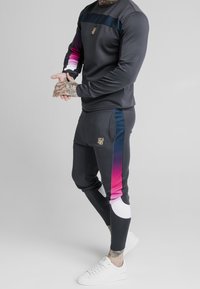 Dunkles Sportset mit verlaufenden pinken Akzenten, einem goldenen Logo auf der Brust und taillierten Hosen mit Seitentaschen und kontrastierenden weißen Details.