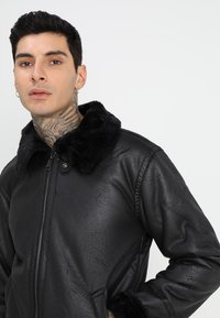Chaqueta de cuero negra con cuello de piel sintética, acabado texturizado, cierre de cremallera y bolsillos laterales; el diseño ajustado realza la silueta.