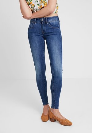 Pantalones vaqueros ajustados en denim azul oscuro con un ligero desgaste, que cuentan con un cierre de cremallera y botón, cinco bolsillos y un diseño sin costuras.