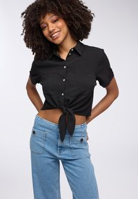Camicetta nera corta con dettagli in stile cravatta; abbinata a jeans a vita alta di un blu chiaro con due tasche frontali.