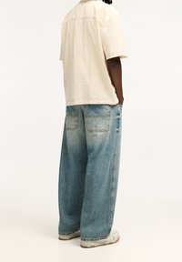 Beige kortärmad skjorta, avslappnad passform. Ljusblå baggy jeans i denim med två bakfickor och en urtvättad textur. Avslappnade sportskor.