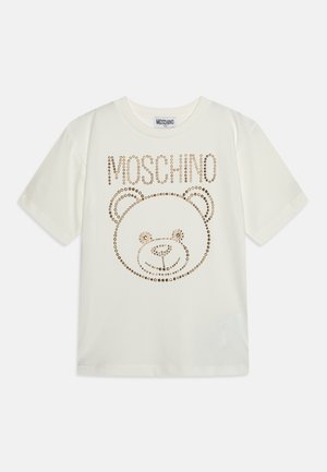 Biała koszulka z krótkim rękawem z pozłacaną twarzą misia i logo "Moschino" nad wzorem z przodu.