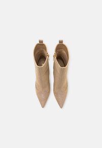 Botines beige de punta afilada con parte superior texturizada, cremalleras en tono dorado y tiradores en la parte trasera. Forro interior suave para mayor comodidad.