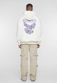 Hvid hættetrøje med lilla sommerfugl grafik på ryggen, parret med beige cargo bukser med klaplommer og en afslappet pasform.