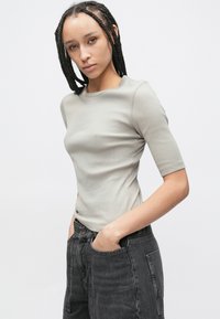 Svetlo siva oprijeta majica iz rebrastega materiala s kratkimi rokavi in okroglim izrezom, v kombinaciji s temno sivimi hlačami z visokim pasom.