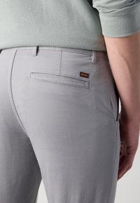 Light grey trousers made of smooth fabric, featuring a sleek design, rear pocket, and an orange "BOSS" logo tag.